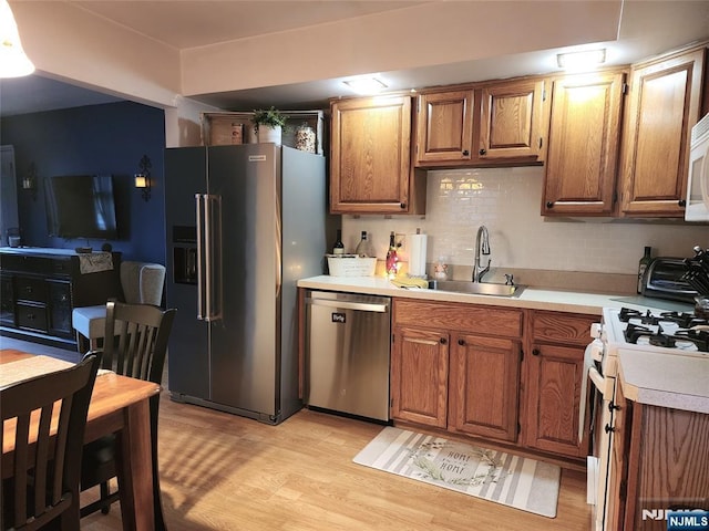 kitchen featuring stainless steel appliances, a sink, light countertops, light wood-style flooring, and backsplash