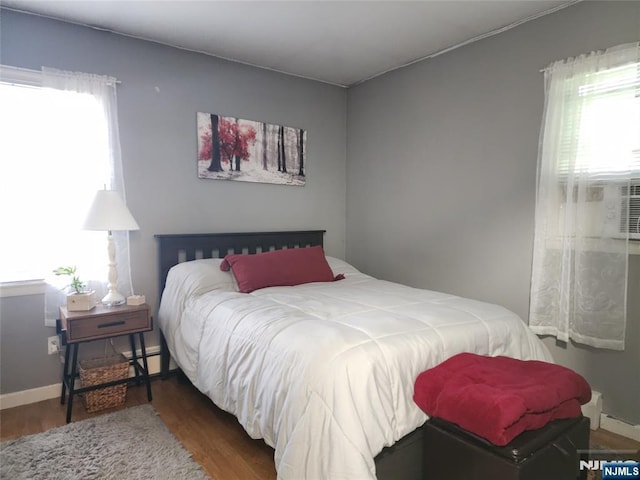 bedroom with multiple windows, wood finished floors, a baseboard radiator, and baseboards