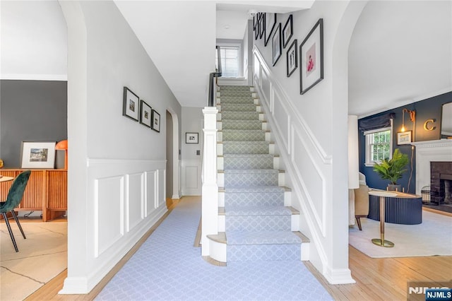stairway with wood finished floors, arched walkways, a healthy amount of sunlight, and a decorative wall