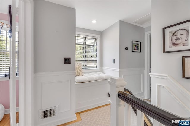 hall featuring a decorative wall, wainscoting, light wood-style flooring, and visible vents