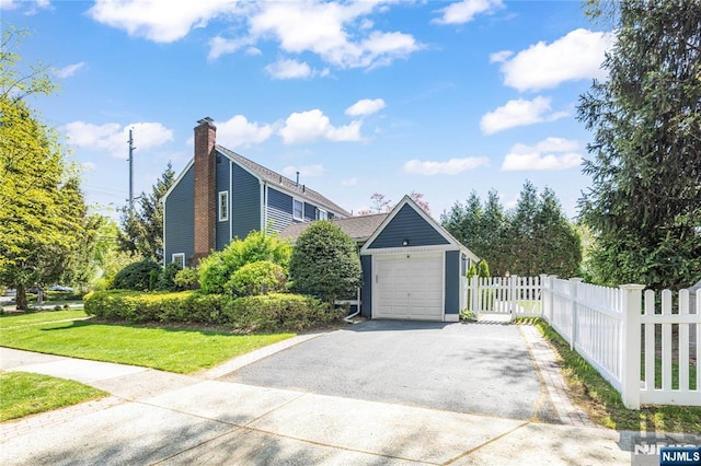 view of side of property with fence, aphalt driveway, a detached garage, a chimney, and a yard