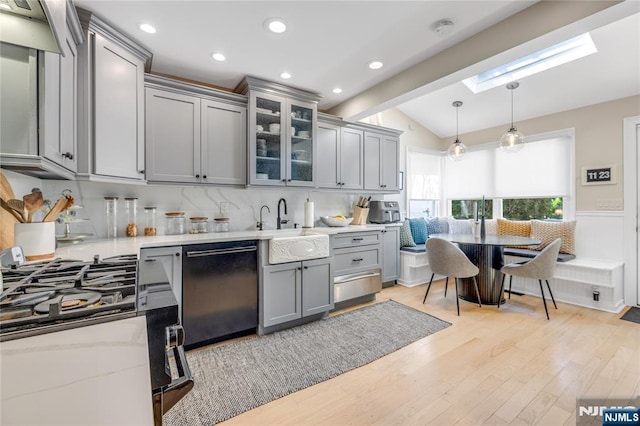 kitchen featuring a sink, light wood finished floors, vaulted ceiling with skylight, gray cabinetry, and dishwashing machine