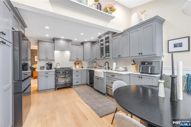 kitchen with light countertops, gray cabinets, high end stove, a sink, and dishwasher