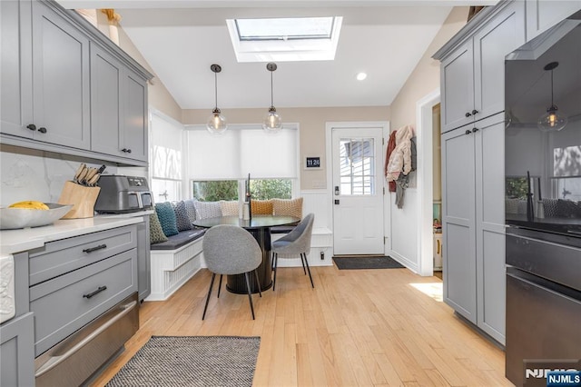 interior space with light wood finished floors, breakfast area, vaulted ceiling with skylight, and gray cabinetry