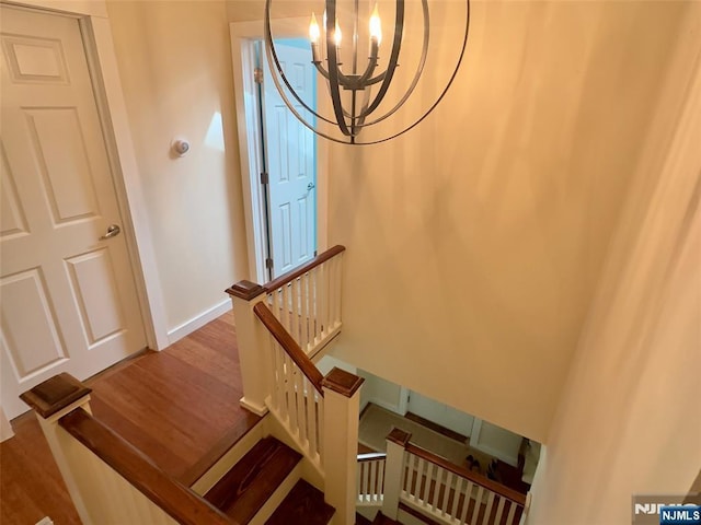 stairs featuring baseboards, wood finished floors, and a chandelier