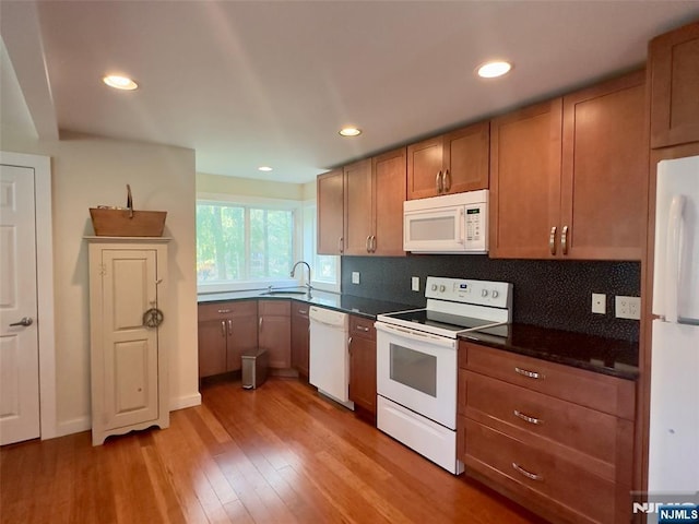kitchen with a sink, dark countertops, light wood-style floors, and white appliances
