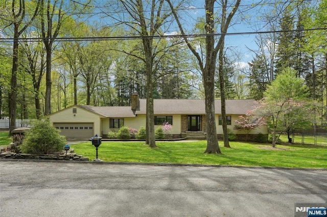 ranch-style house with an attached garage, fence, a chimney, and a front lawn