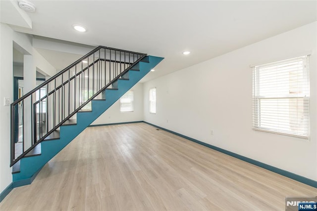 unfurnished living room featuring stairs, baseboards, and wood finished floors