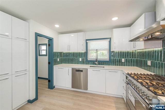 kitchen featuring a sink, appliances with stainless steel finishes, a healthy amount of sunlight, and wall chimney range hood