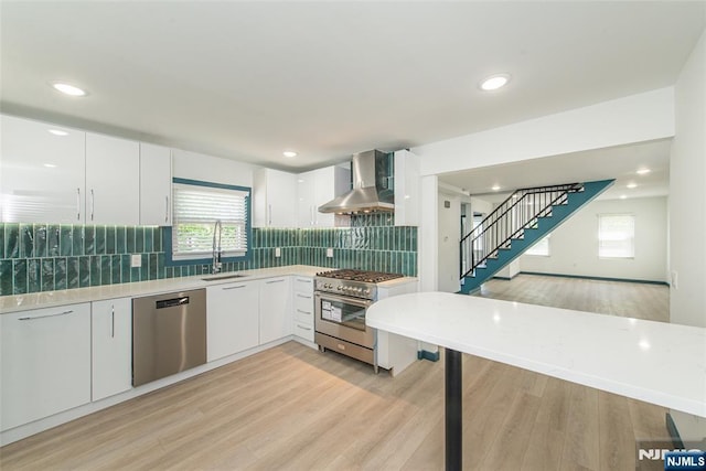 kitchen with light wood-style floors, wall chimney exhaust hood, white cabinetry, and stainless steel appliances