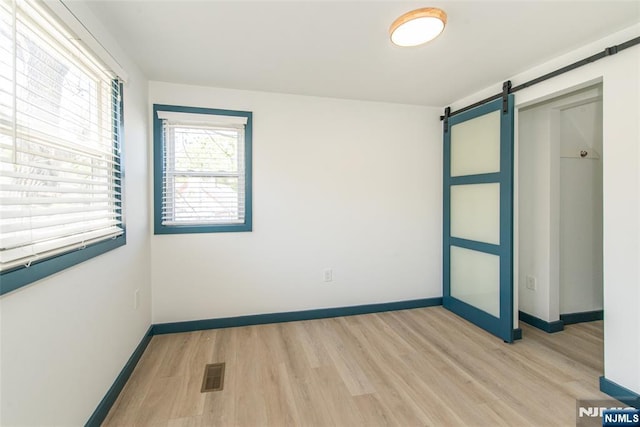 spare room featuring visible vents, a barn door, baseboards, and light wood-type flooring