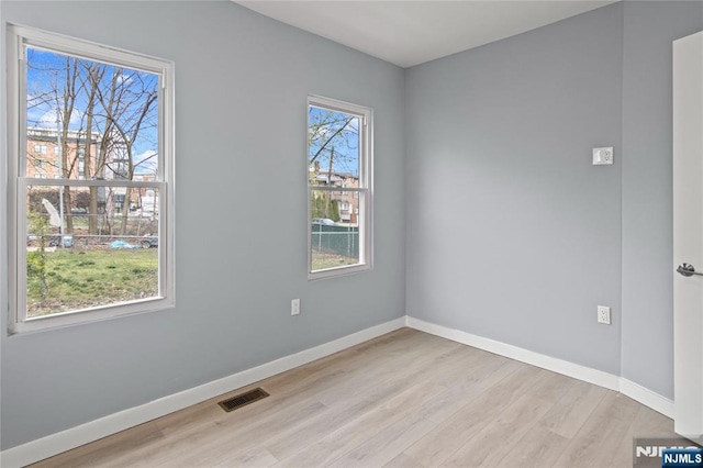 empty room featuring visible vents, light wood finished floors, and baseboards