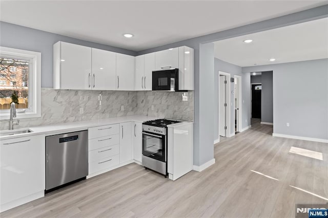 kitchen with light countertops, white cabinets, a sink, light wood-style flooring, and stainless steel appliances