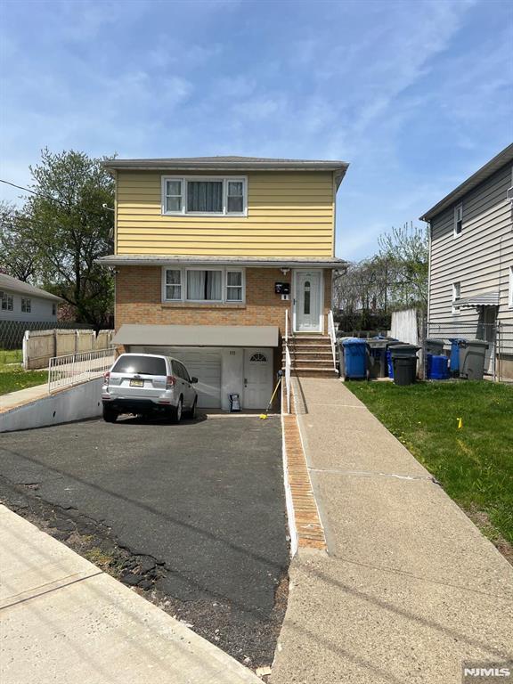 view of front of property featuring driveway, a garage, brick siding, fence, and entry steps