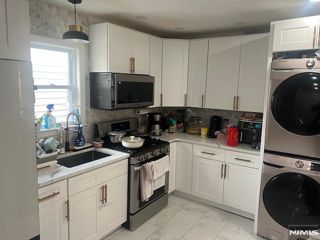 kitchen with stacked washer / dryer, appliances with stainless steel finishes, a sink, white cabinets, and marble finish floor