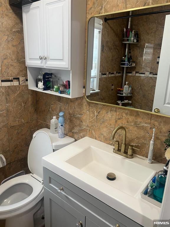 bathroom with toilet, tile walls, decorative backsplash, and vanity