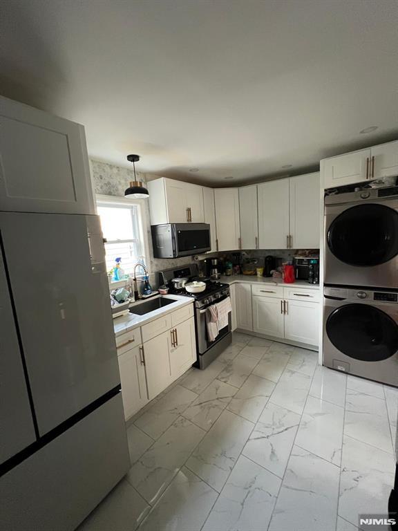 kitchen with stacked washer and dryer, refrigerator, gas stove, a sink, and stainless steel microwave