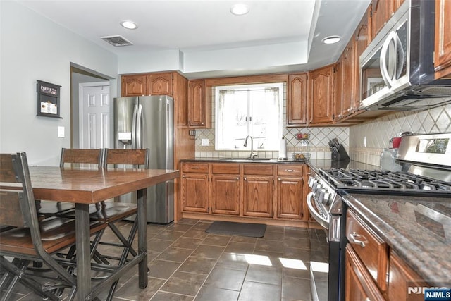 kitchen featuring visible vents, tasteful backsplash, brown cabinets, a sink, and stainless steel appliances
