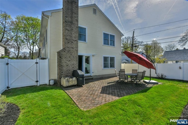 rear view of house with a fenced backyard, a gate, a chimney, and a lawn