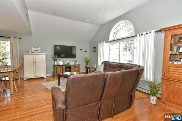 living area with baseboard heating, a wealth of natural light, lofted ceiling, and light wood-style floors