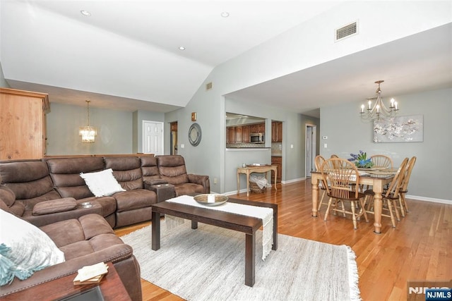 living area featuring visible vents, light wood-style flooring, a notable chandelier, and vaulted ceiling