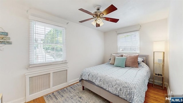 bedroom featuring baseboards, multiple windows, a ceiling fan, and wood finished floors