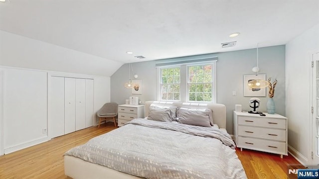 bedroom with visible vents, wood finished floors, lofted ceiling, and a closet