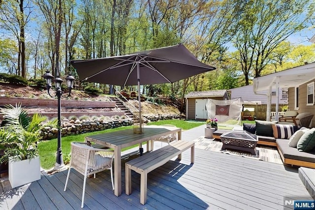 wooden terrace with fence, outdoor dining space, an outdoor living space with a fire pit, a shed, and an outdoor structure