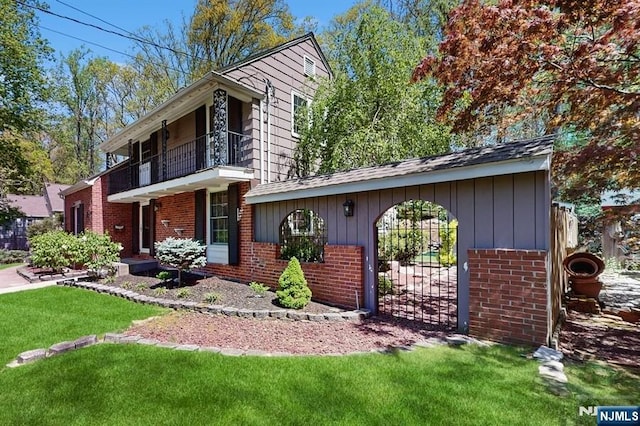 view of front of home featuring brick siding, a gate, a balcony, and a front yard