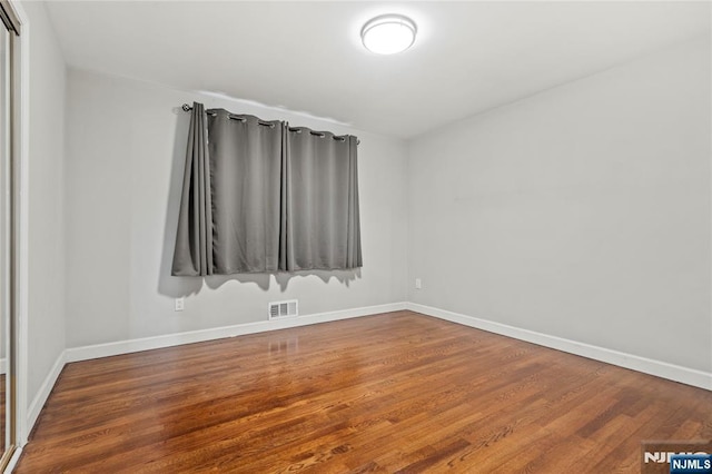 unfurnished room featuring baseboards, visible vents, and wood finished floors