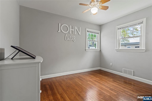 spare room with a ceiling fan, visible vents, wood finished floors, and baseboards
