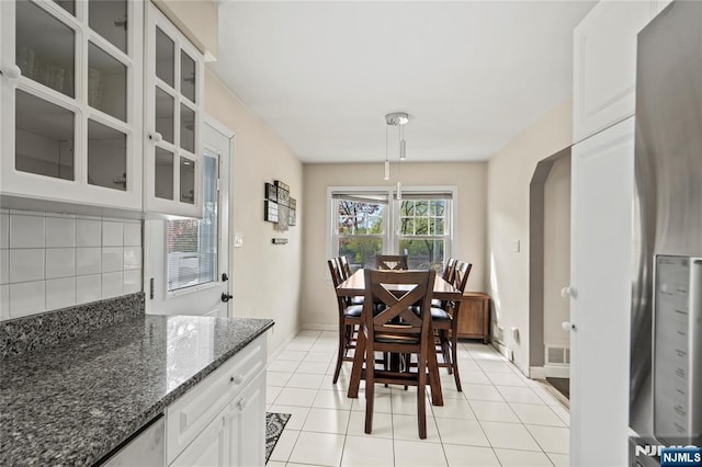 dining area featuring baseboards, visible vents, light tile patterned floors, and arched walkways