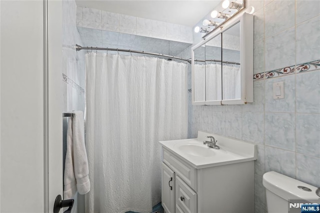 bathroom with tile walls, curtained shower, toilet, and vanity