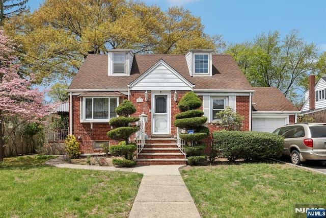 new england style home with roof with shingles, a front lawn, brick siding, and a garage