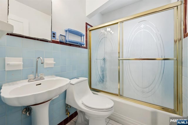 full bath featuring a sink, toilet, shower / bath combination with glass door, and tile walls