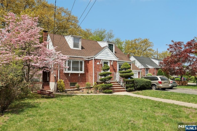 view of front of property with a front lawn, a shingled roof, brick siding, aphalt driveway, and a chimney