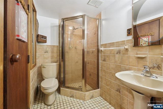 full bath with tile walls, a wainscoted wall, toilet, visible vents, and a stall shower