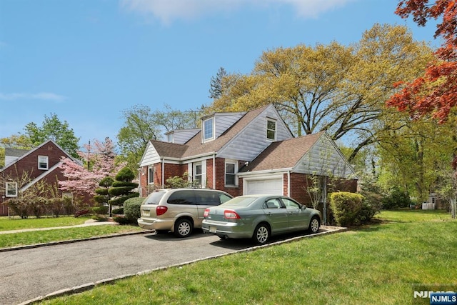 view of front of property featuring brick siding, aphalt driveway, a shingled roof, a garage, and a front yard