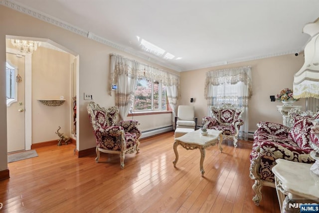 sitting room with baseboard heating, light wood-type flooring, crown molding, and baseboards