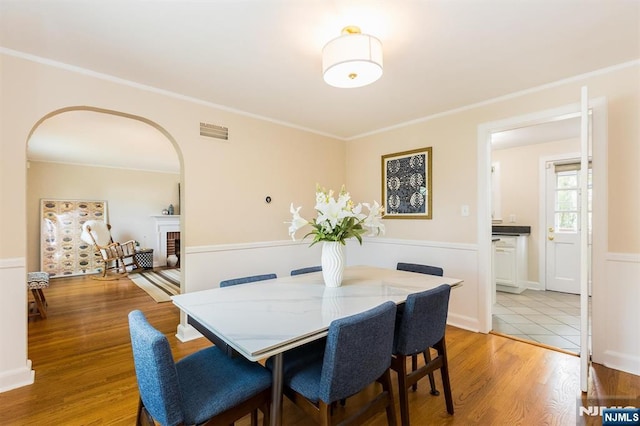 dining room featuring ornamental molding, arched walkways, visible vents, and light wood-style floors
