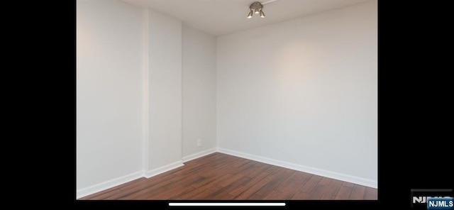 spare room with dark wood-type flooring and baseboards