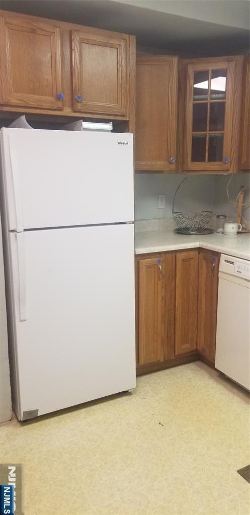 kitchen featuring light floors, white appliances, glass insert cabinets, light countertops, and brown cabinets