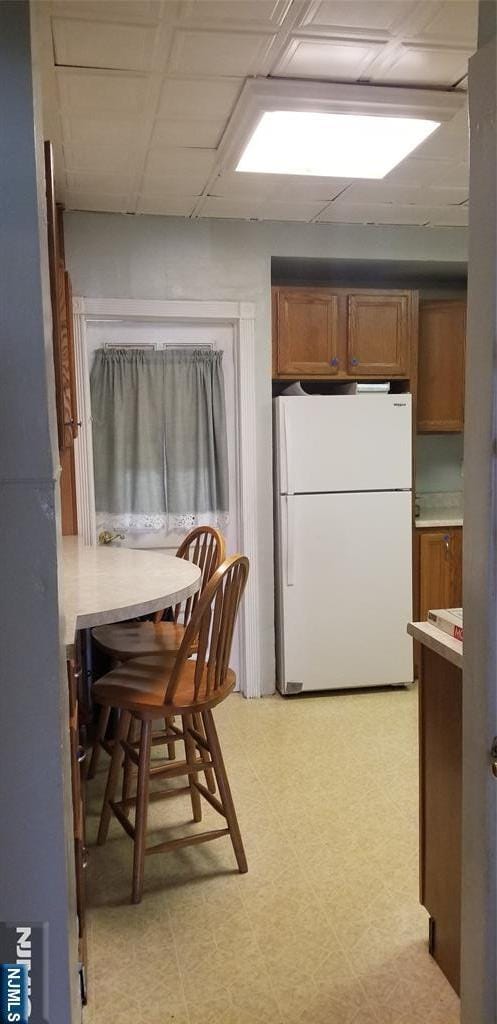 kitchen featuring light floors, brown cabinetry, light countertops, and freestanding refrigerator