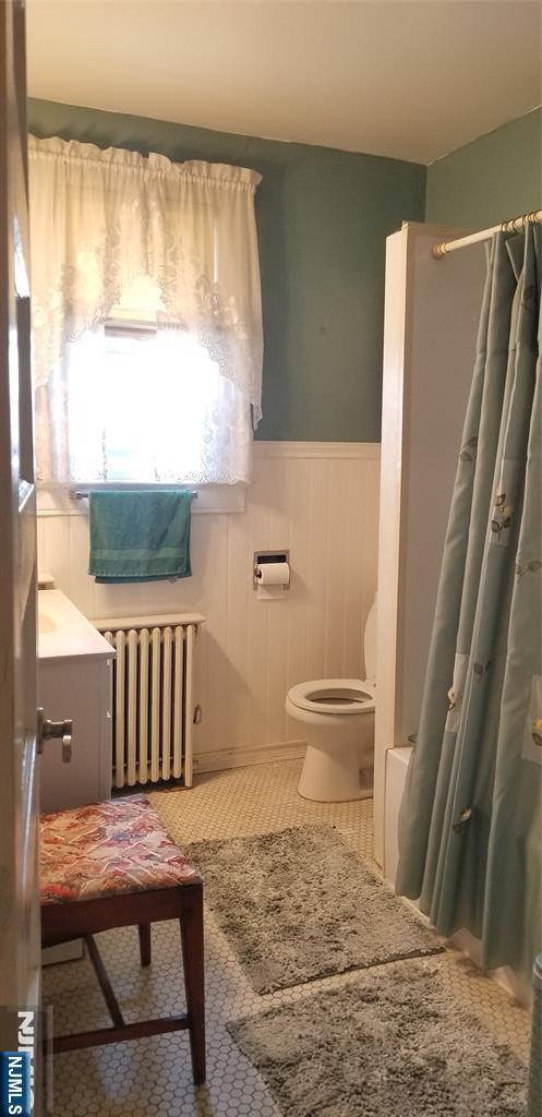 bathroom with curtained shower, toilet, a wainscoted wall, and radiator