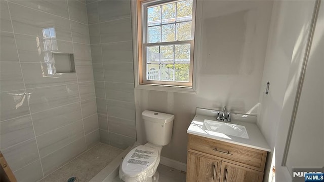 bathroom featuring toilet, a tile shower, and vanity