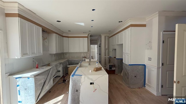 kitchen with light stone countertops, a sink, light wood-style flooring, ornamental molding, and white cabinets