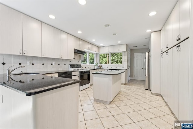 kitchen featuring a sink, freestanding refrigerator, a peninsula, under cabinet range hood, and gas range oven