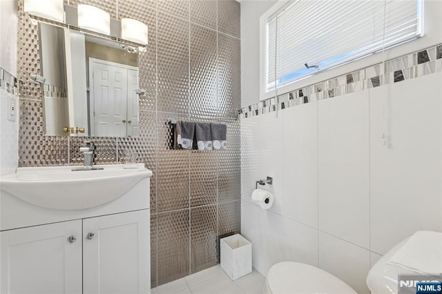 bathroom with tile patterned flooring, vanity, toilet, and tile walls