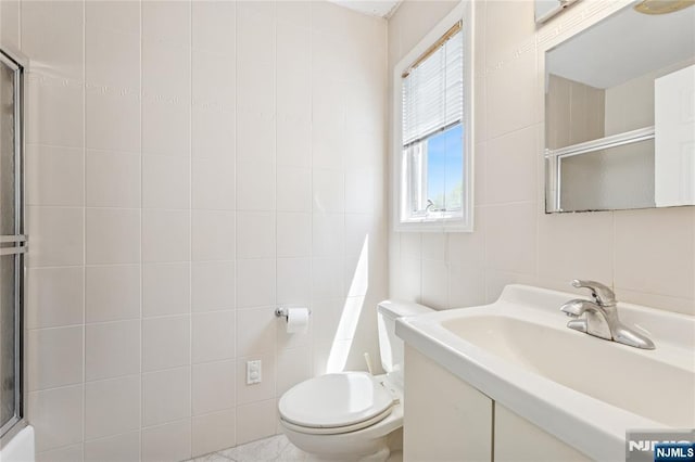 bathroom with toilet, tile walls, a shower with shower door, and vanity