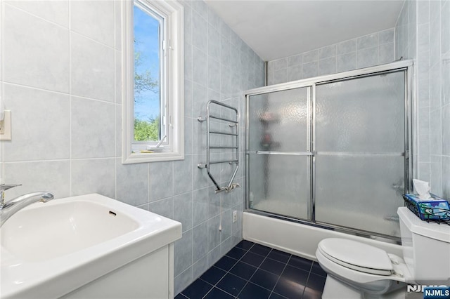 full bath with tile patterned flooring, shower / bath combination with glass door, toilet, tile walls, and a sink